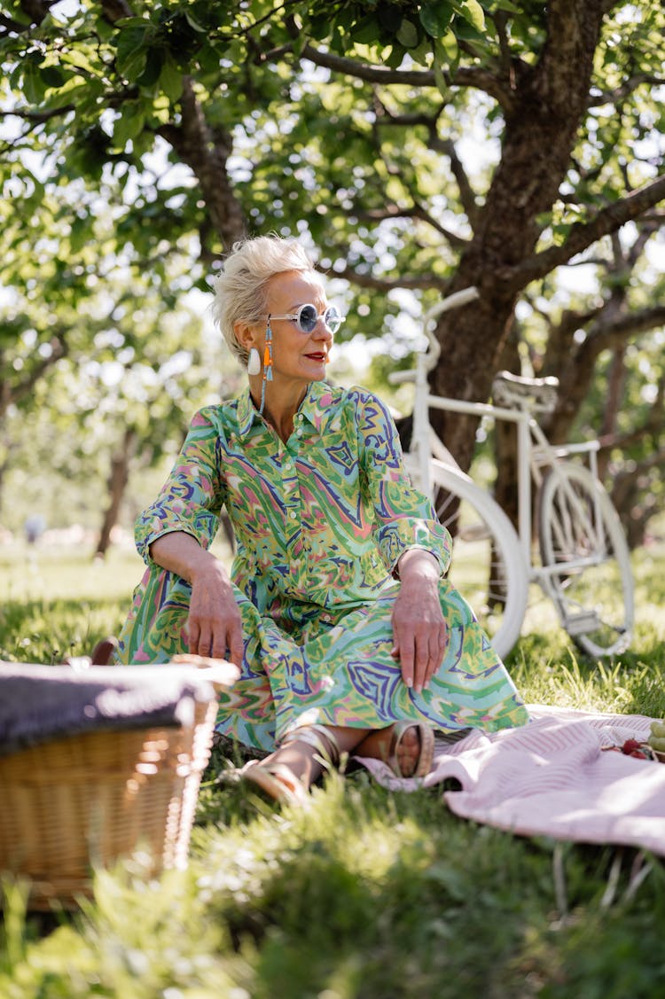 An Elderly Woman In A Printed Dress Sitting At A Park