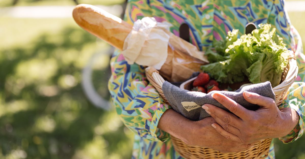 A person holding a smartphone with a QR code over a basket of fresh vegetables at a farmer's market