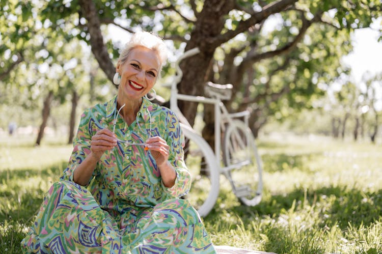 A Happy Elderly Woman In A Printed Dress Sitting At A Park