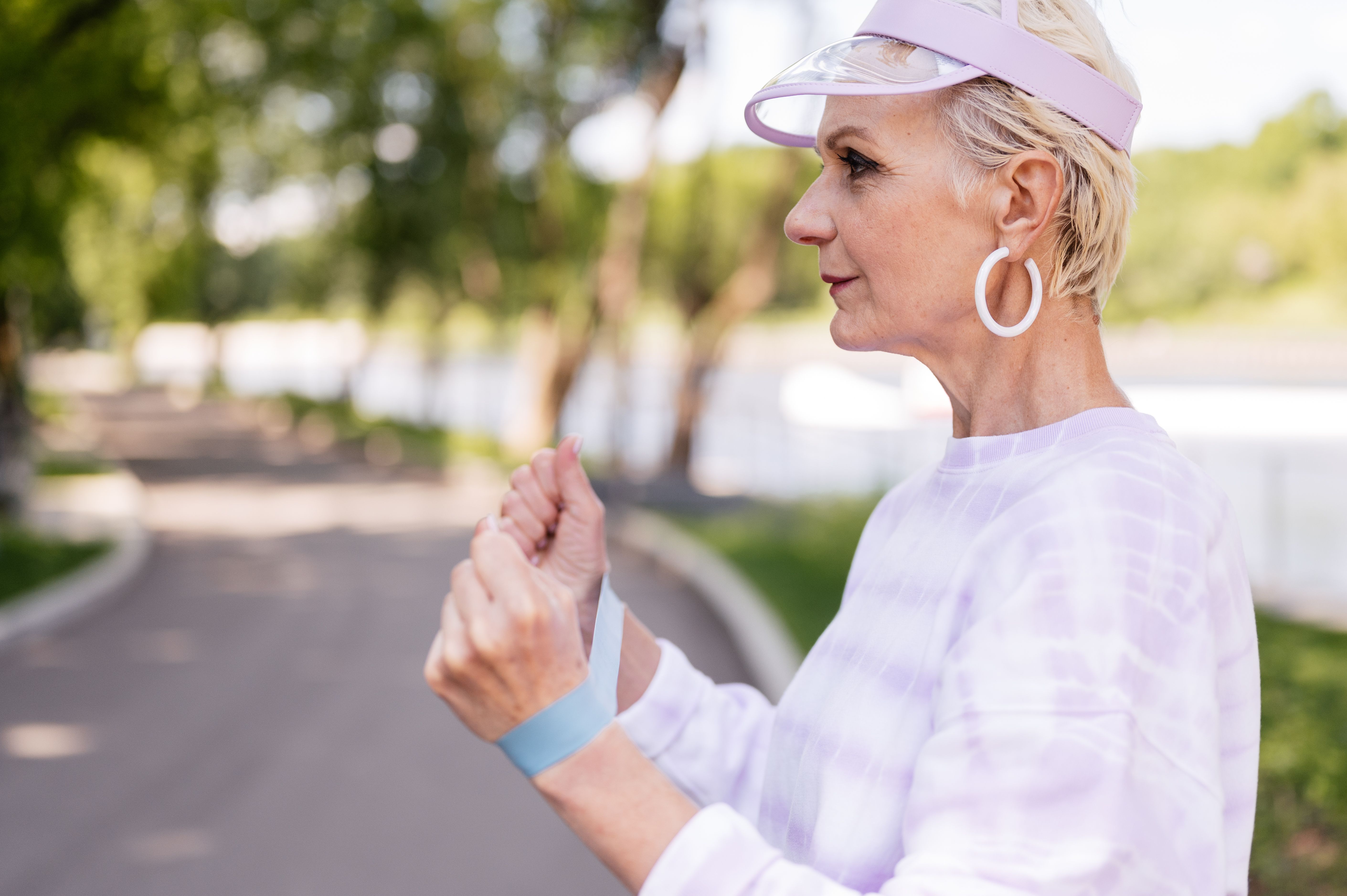 Elderly woman exercising with resistance band in a sunny park setting, promoting a healthy lifestyle.