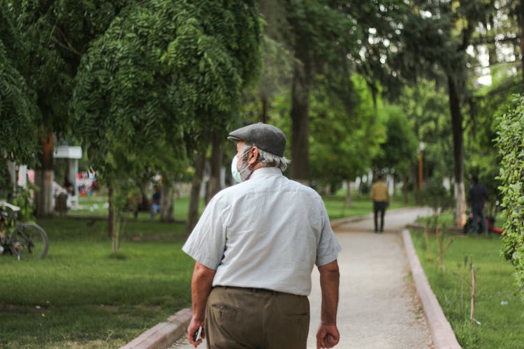 Unrecognizable Citizen In Medical Mask Walking On Pavement In Park