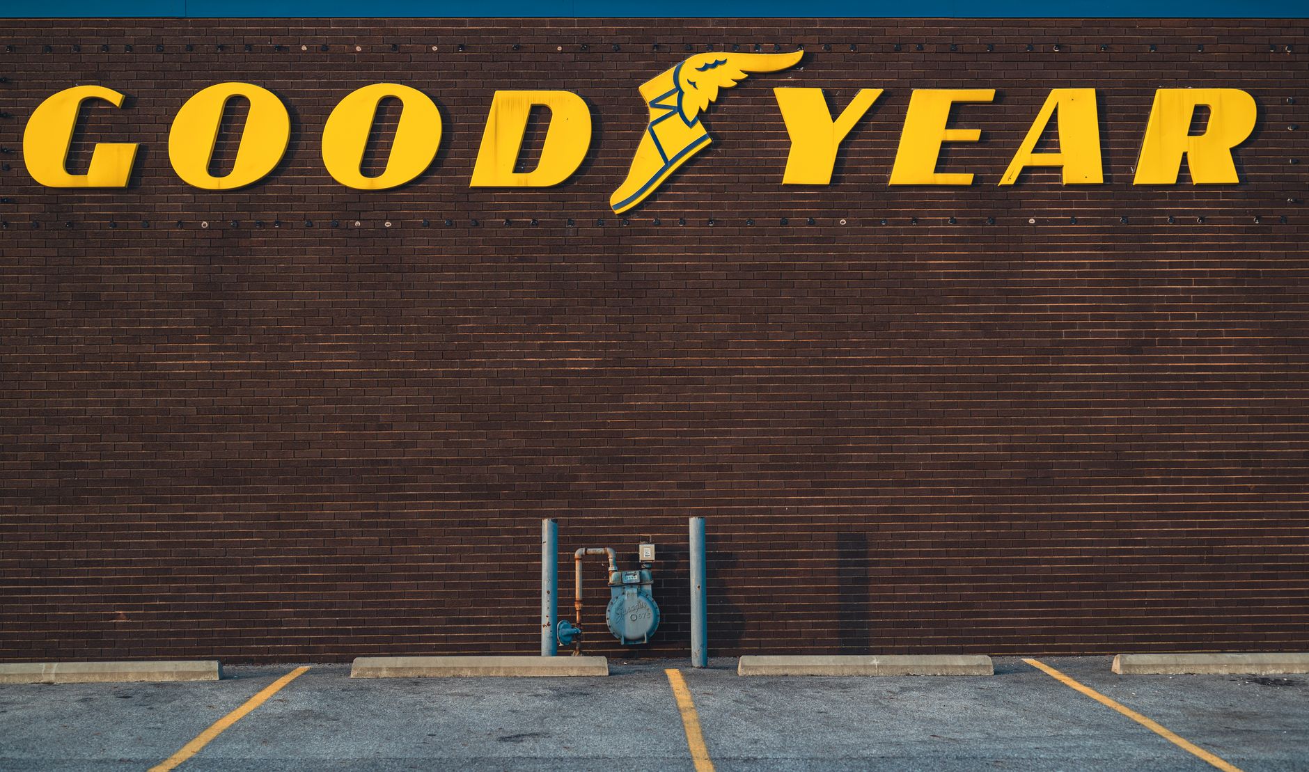 A brick wall featuring a Goodyear sign above an empty parking lot.