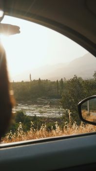 View of a serene rural landscape through a car window during sunset, highlighting nature's tranquility.