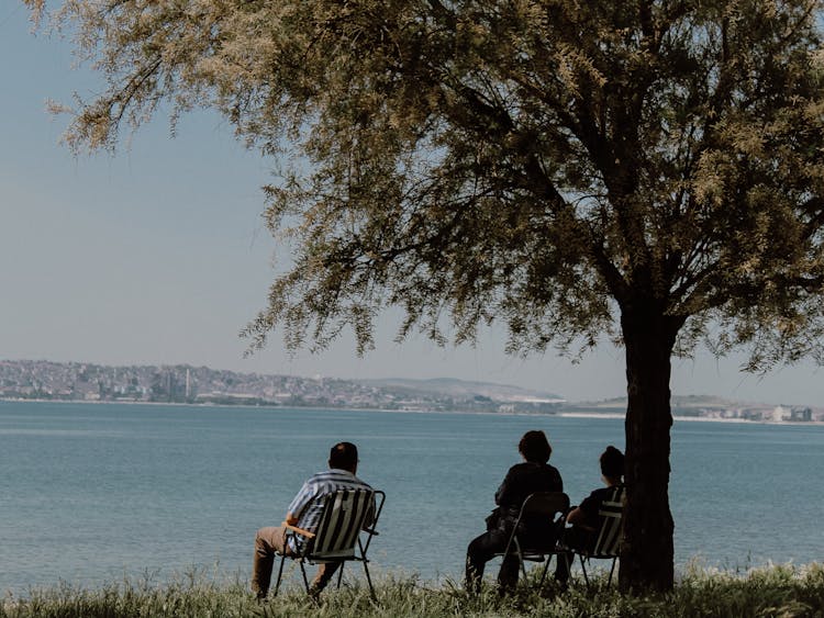 People Sitting On Chairs Near Body Of Water