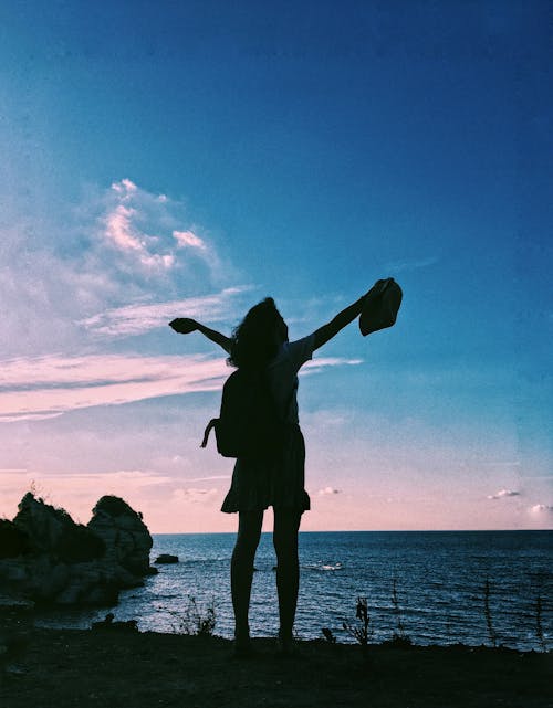 Silhouette of a Woman Standing with her Arms Raised near the Ocean