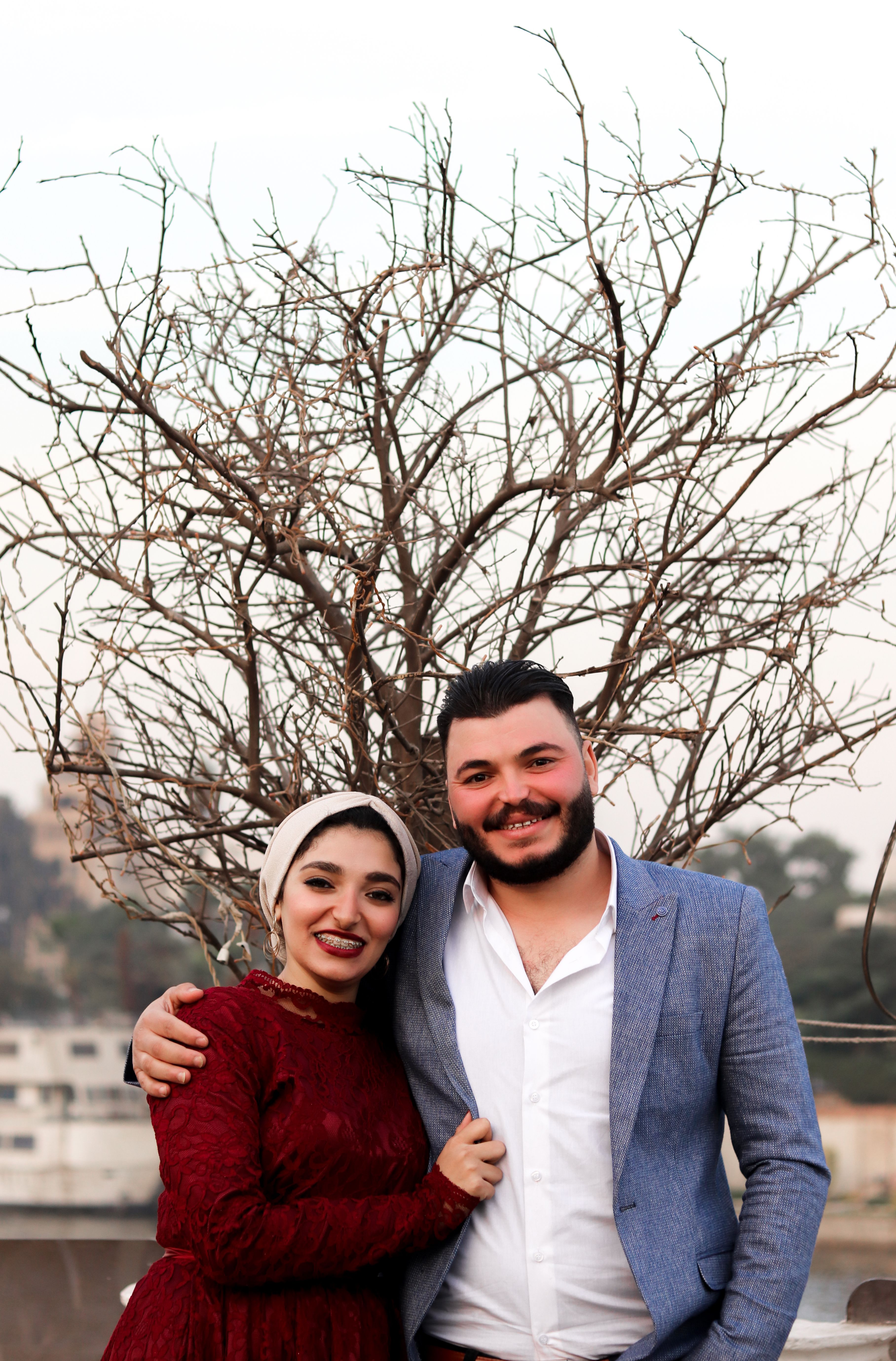 A joyful couple embracing by a tree during daylight in an urban setting.