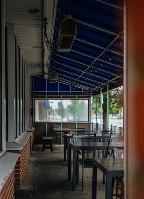 Free Quiet outdoor dining area with tables and chairs under a blue awning, ready for guests. Stock Photo