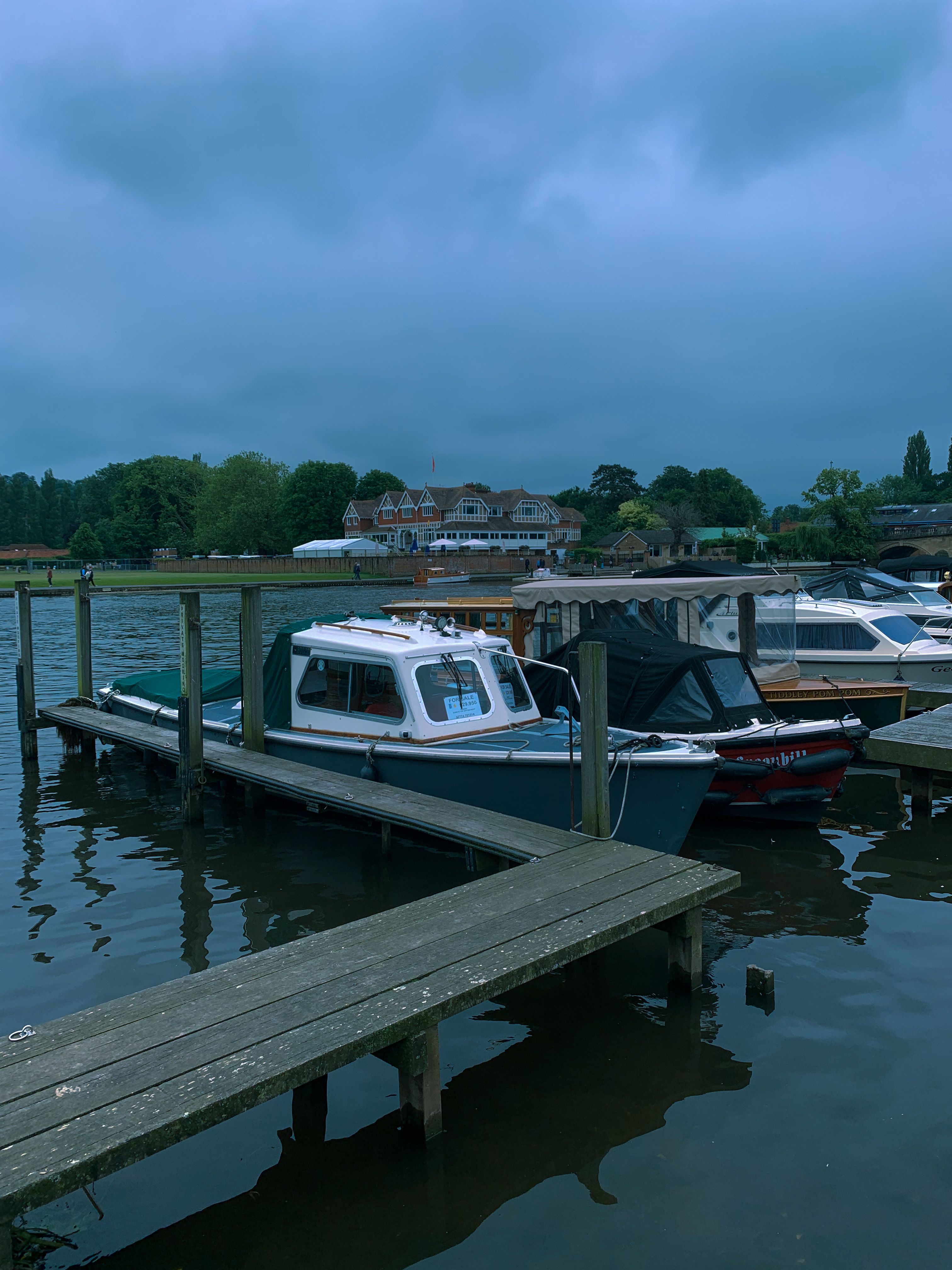 Serene view of boats moored at a lakeside dock during twilight with a scenic backdrop of nature and houses.