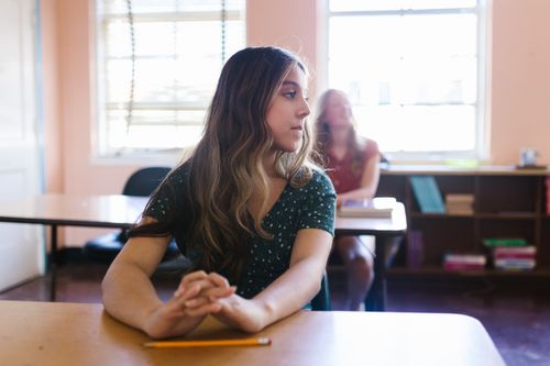 Free A student sitting thoughtfully in a sunlit classroom with bookshelves in the background. Stock Photo