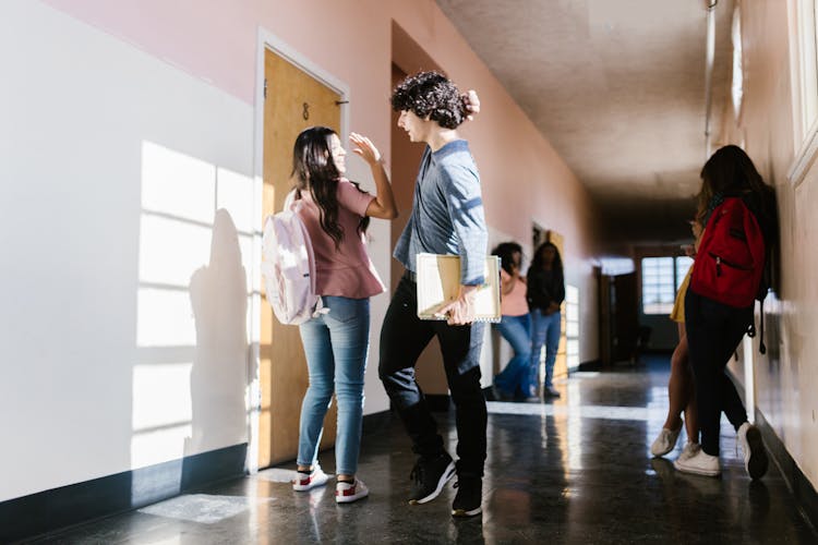 Two Students Giving High Five In School Hallway