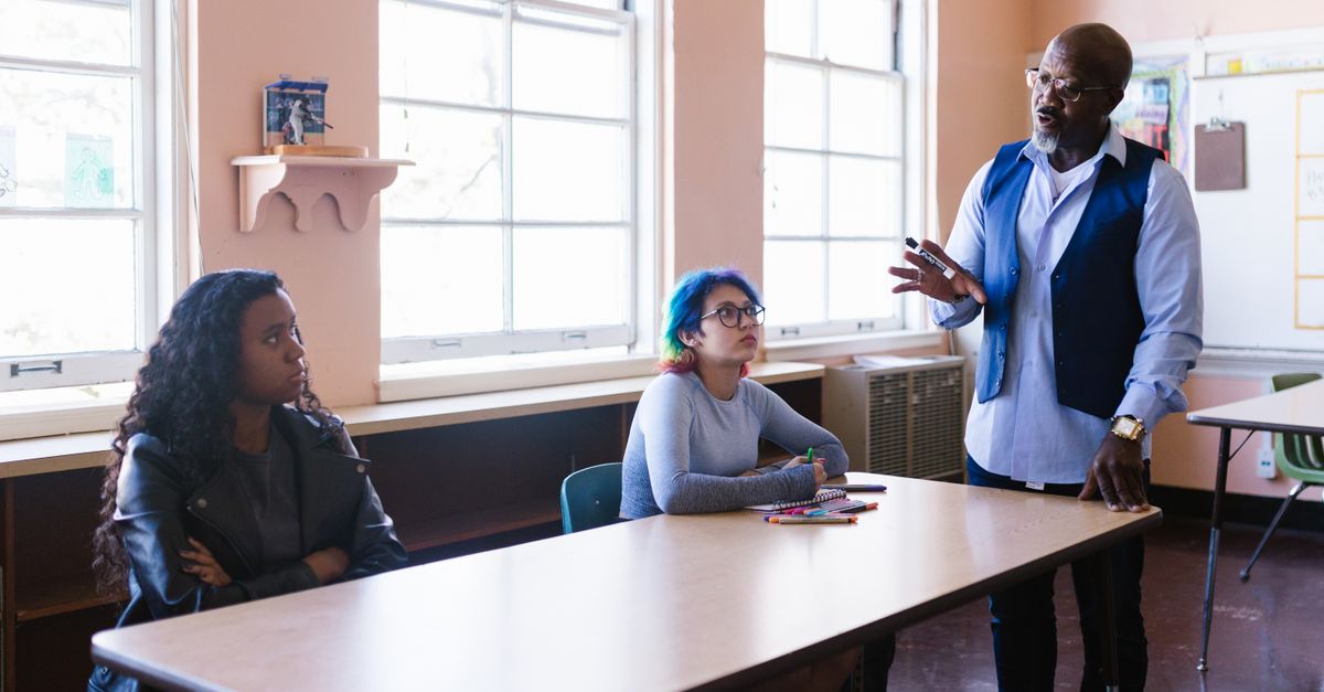 a teacher smiling while talking with students in a bright classroom