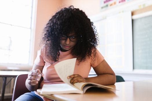 Young woman with curly hair studies in a classroom, focused on her book.