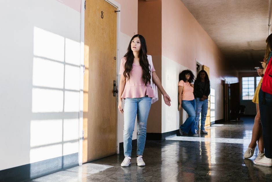 New student looking isolated in school hallway while other students watch