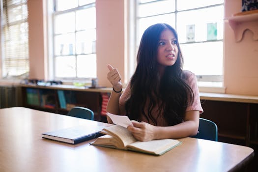 Young woman in classroom reading and contemplating with an open book on the desk.