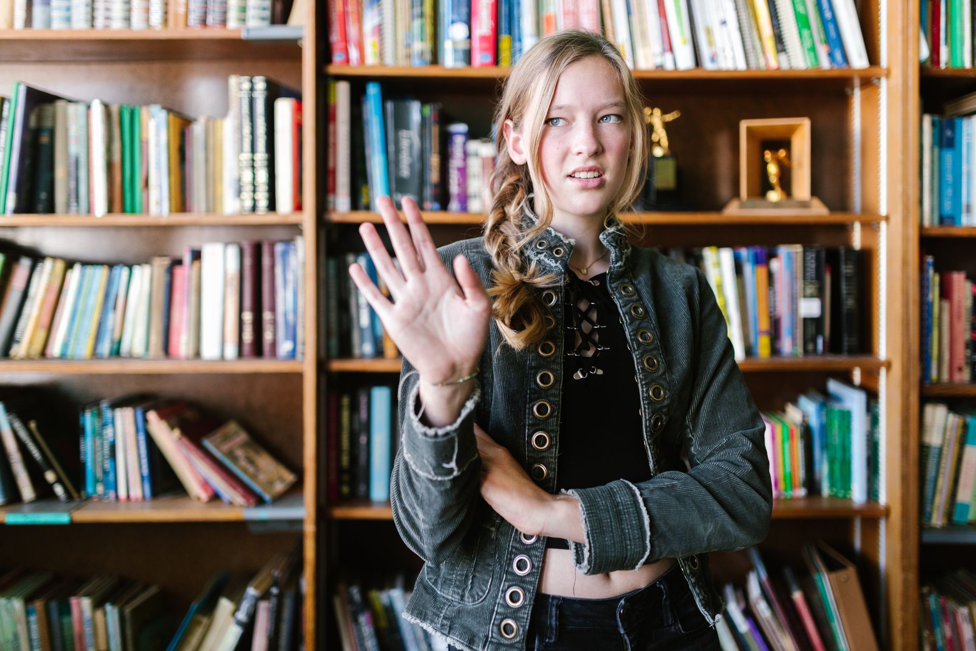 Teen girl in denim jacket dismissing gesture in a library setting.