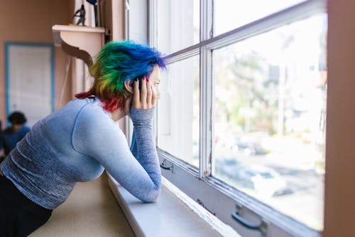 Woman in Blue Long Sleeve Shirt Near Glass Window