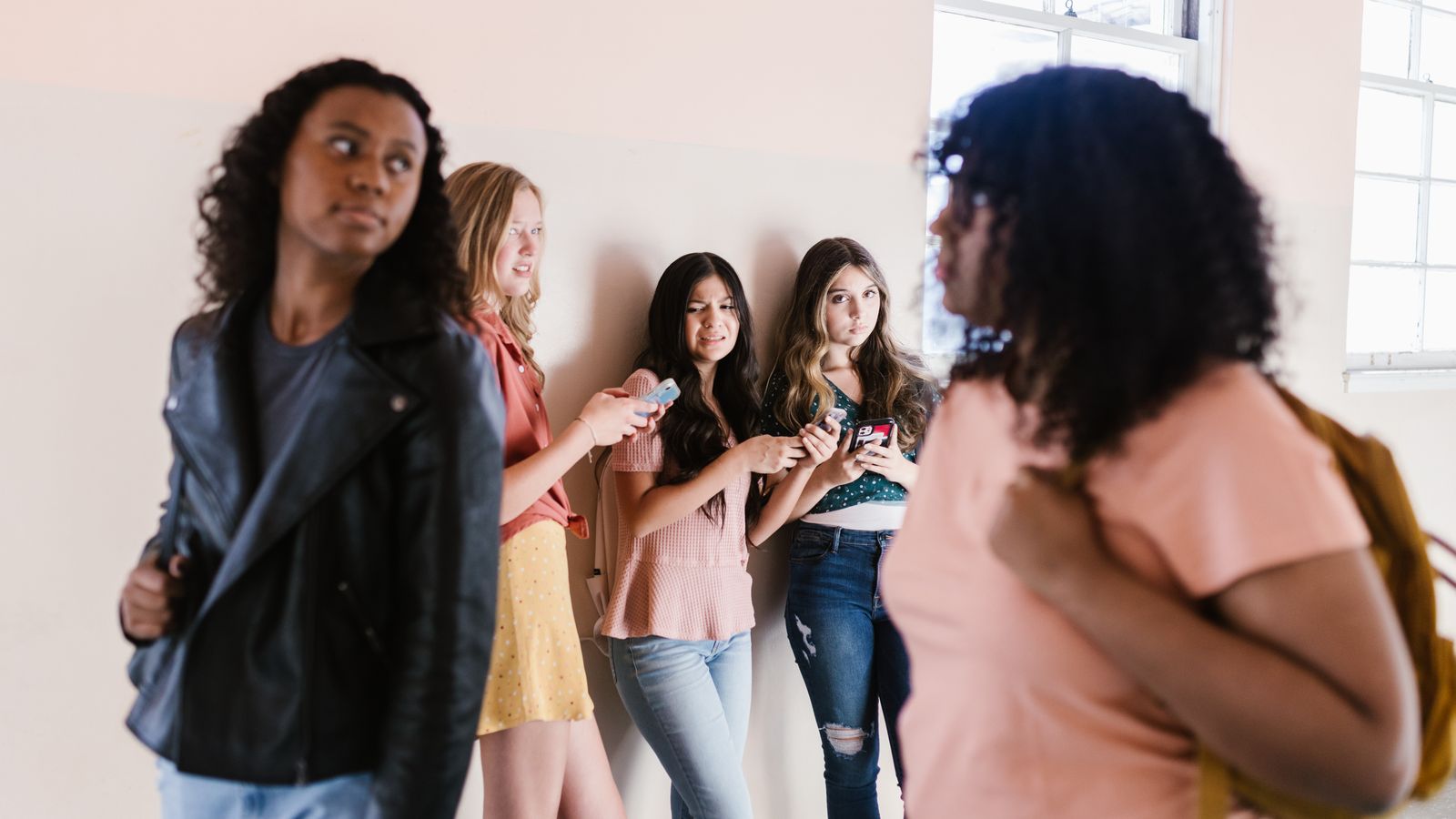 Group of diverse teenagers hanging out in a school hallway, chatting and enjoying each other's company.