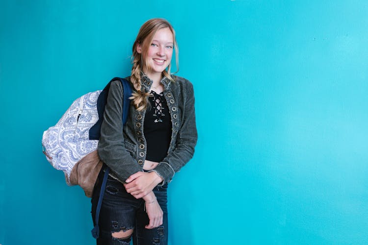 Woman Carrying A Backpack Standing Beside  A Blue Wall