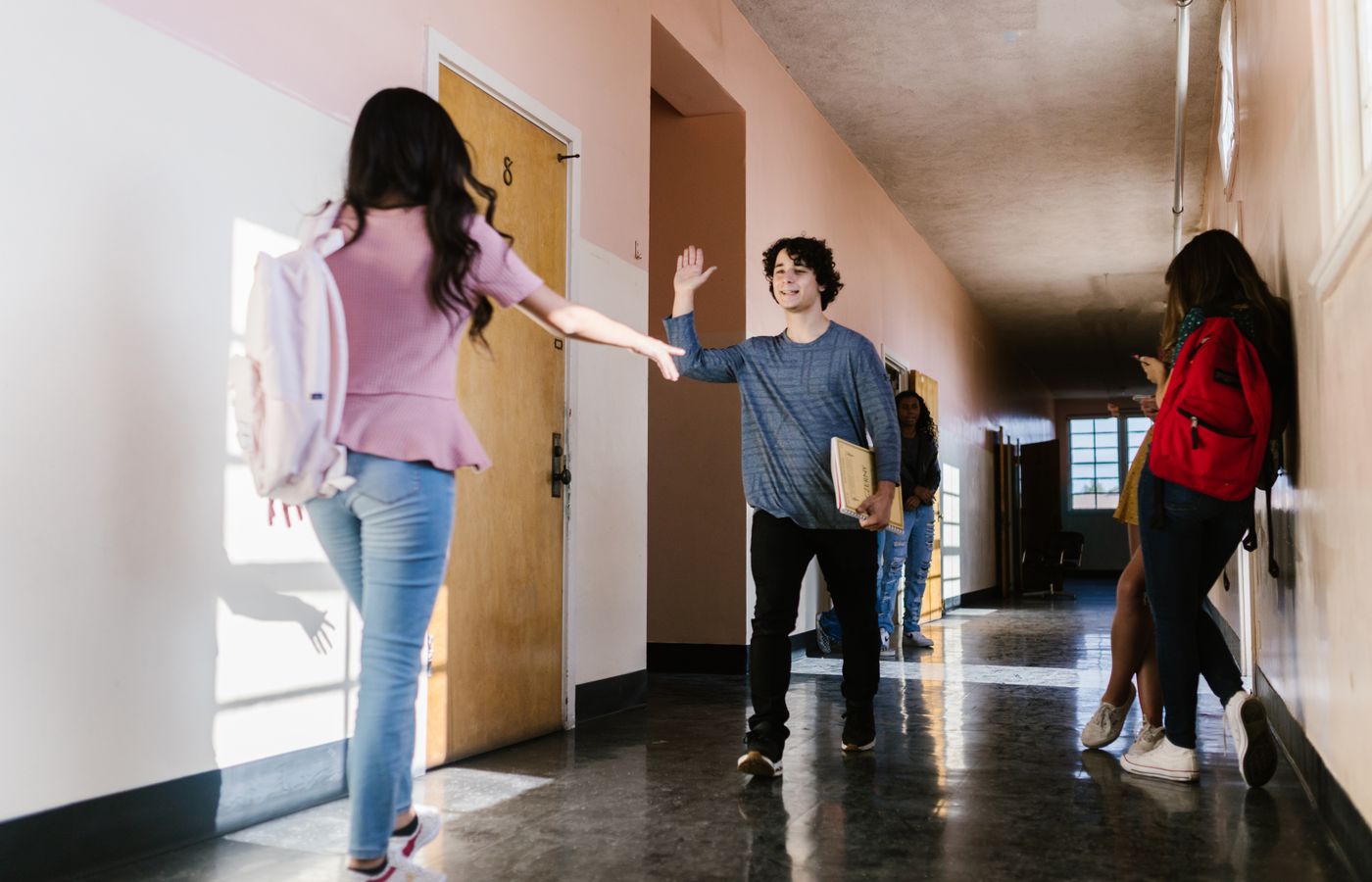 Teens greeting each other happily in a school hallway with natural light.
