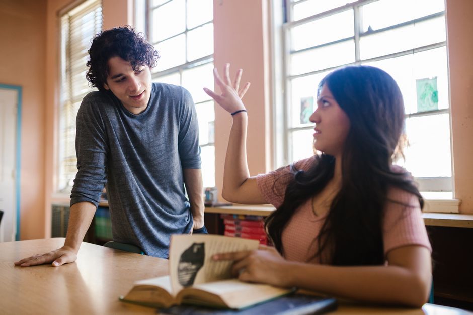 Two students engaged in a lively discussion in a sunlit classroom.