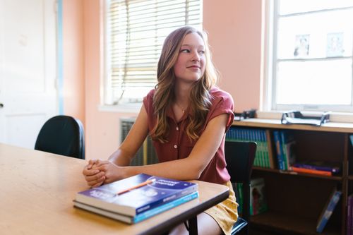 Free A young adult woman sitting at a desk in a classroom with textbooks and looking thoughtful. Stock Photo