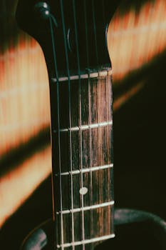 A detailed close-up of an acoustic guitar's fretboard highlighting its wooden texture and strings under natural lighting.
