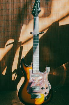 Electric guitar with sunlight casting dramatic shadows on a bamboo backdrop.