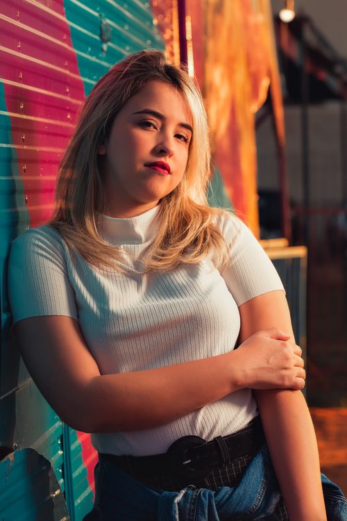 Free Stylish young woman in white top leans against a colorful corrugated wall, capturing a pensive and modern vibe. Stock Photo