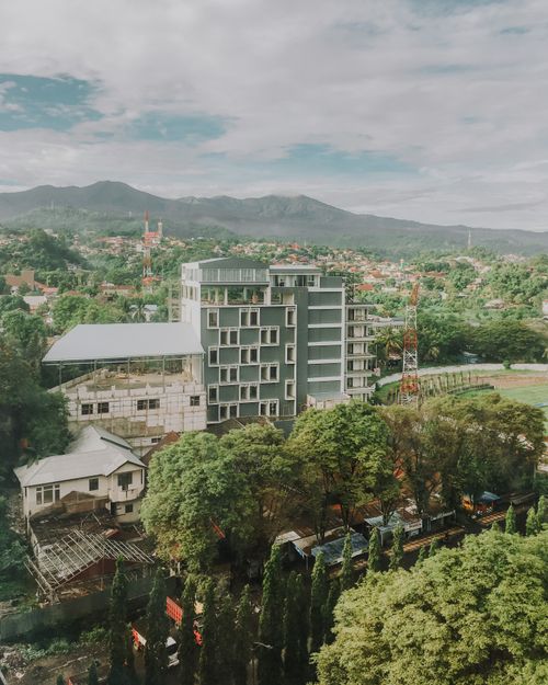 Free An aerial shot of a modern building surrounded by mountains and lush greenery under a cloudy sky. Stock Photo