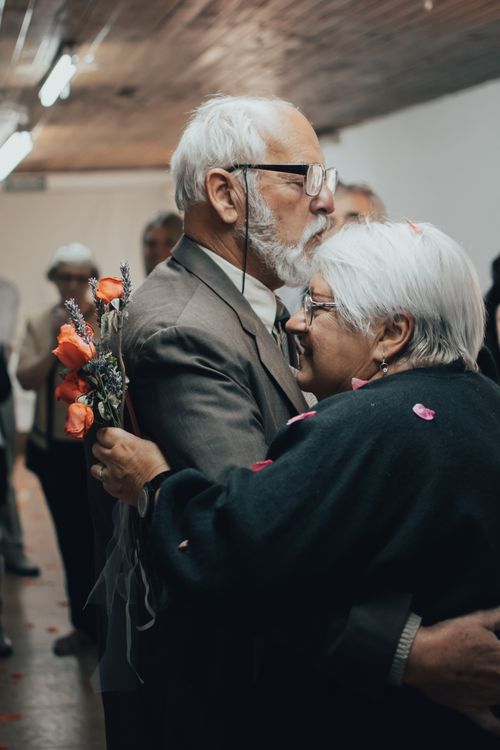Free Elderly couple embracing with a bouquet of roses indoors, expressing love and comfort. Stock Photo