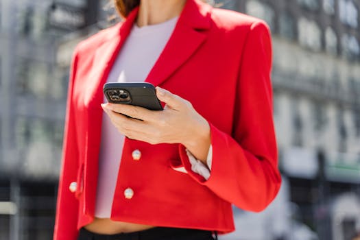 A fashionable woman wearing a red blazer using a smartphone in an urban outdoor setting.