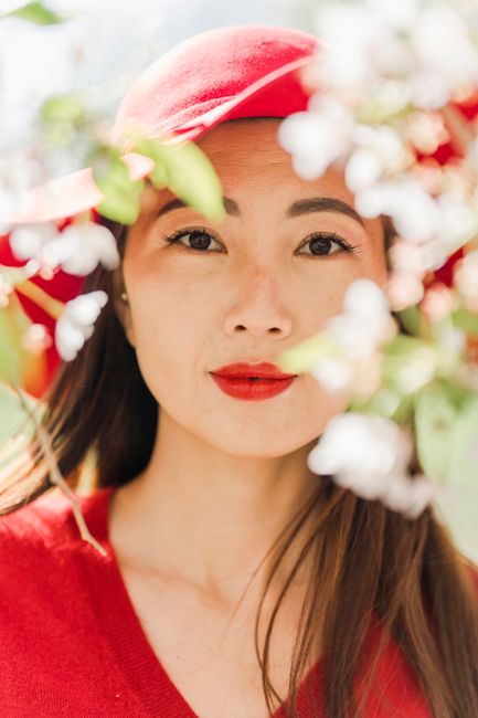 Portrait of a fashionable woman in a red hat, surrounded by ethereal white blossoms.