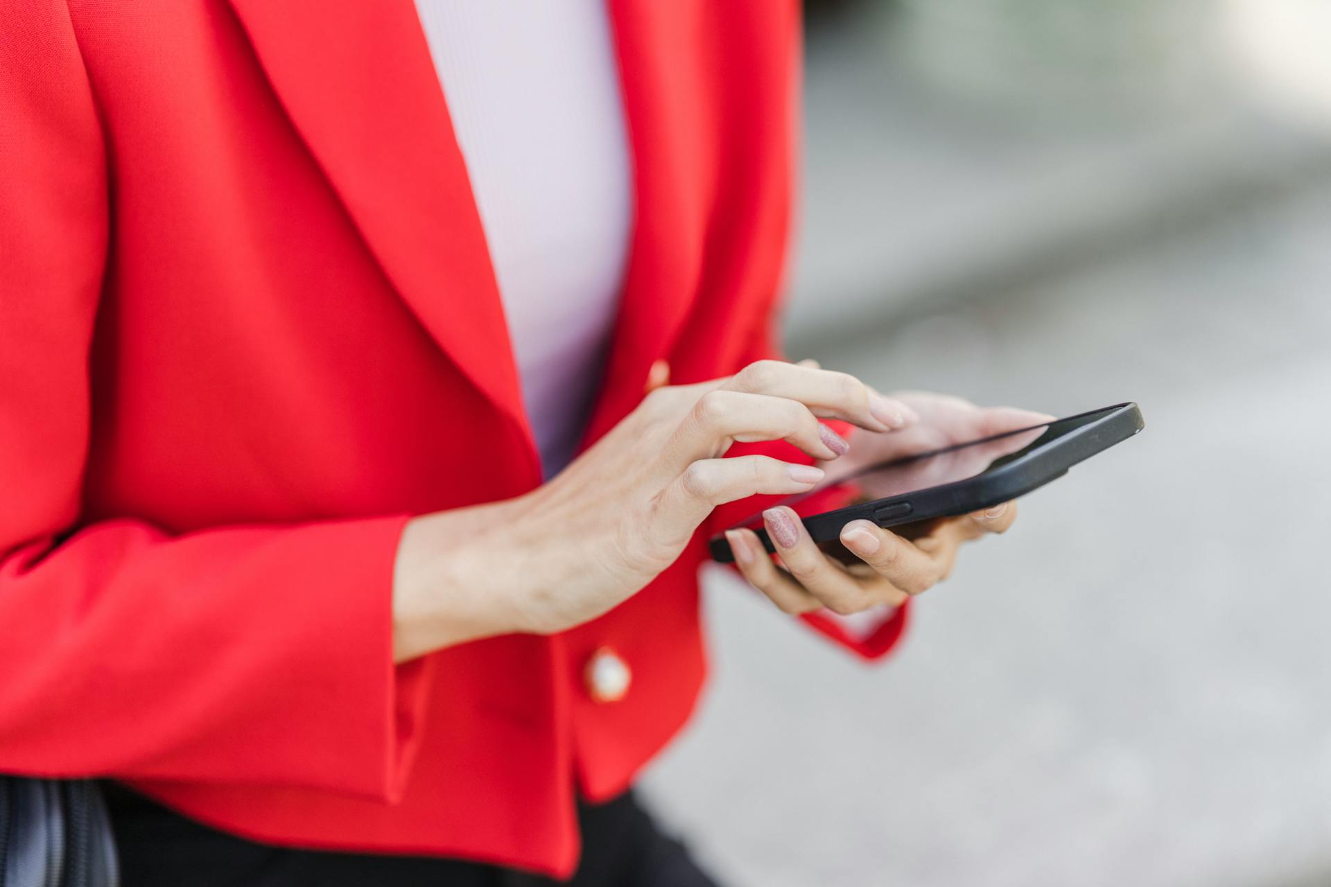 A woman in a red blazer using a smartphone, engaged in mobile technology.