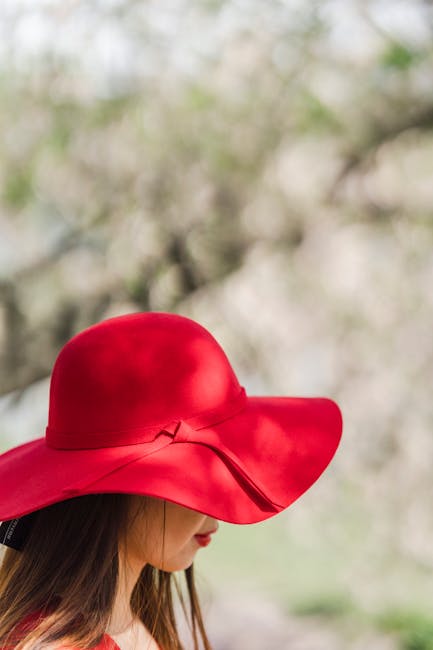 Profile view of a woman wearing a vibrant red sun hat with a blurred nature background.