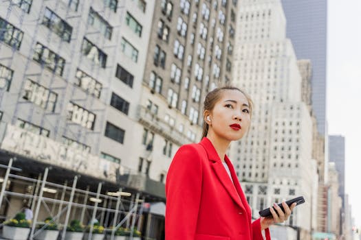 Stylish woman in a red blazer holding a smartphone in a bustling city street.