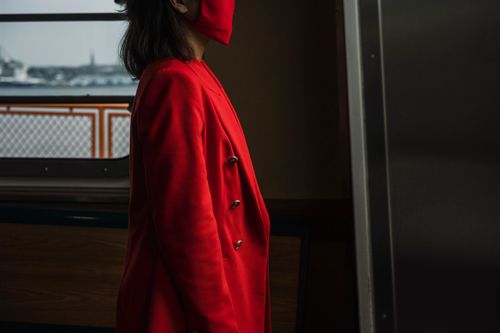 Free A woman in a red blazer and mask stands indoors near a window. Stock Photo