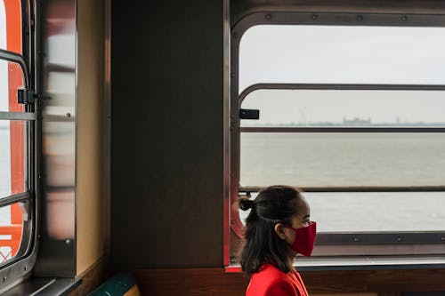 Woman Wearing a Red Face Mask Sitting by the Window
