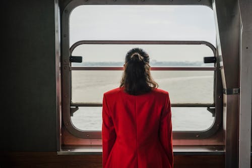 Woman in Red Suit Standing by the Window