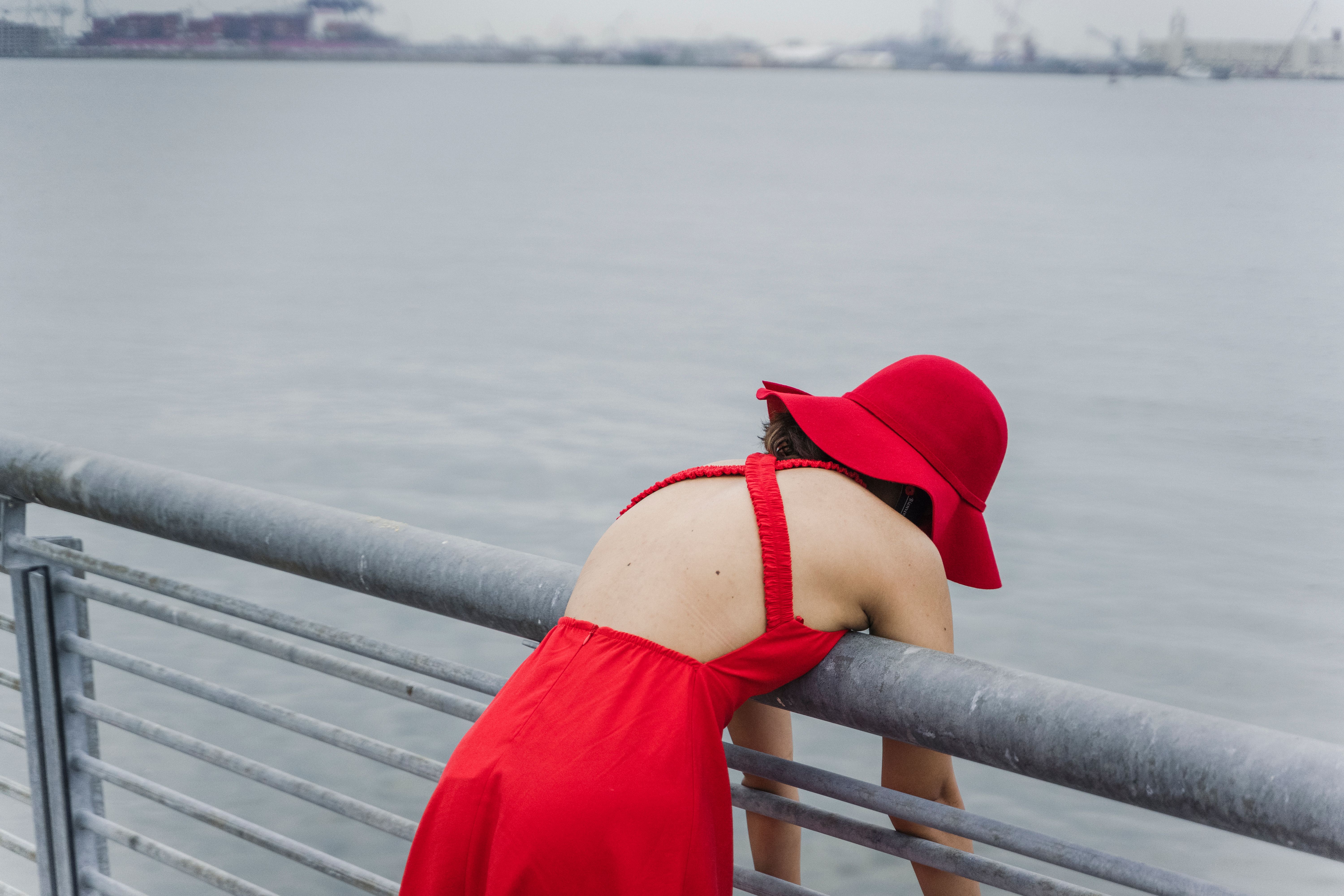 Woman in Red Dress and Sun Hat Leaning on Metal Railings · Free Stock Photo