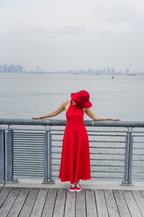Woman in Red Dress and Sun Hat Leaning on Metal Railings