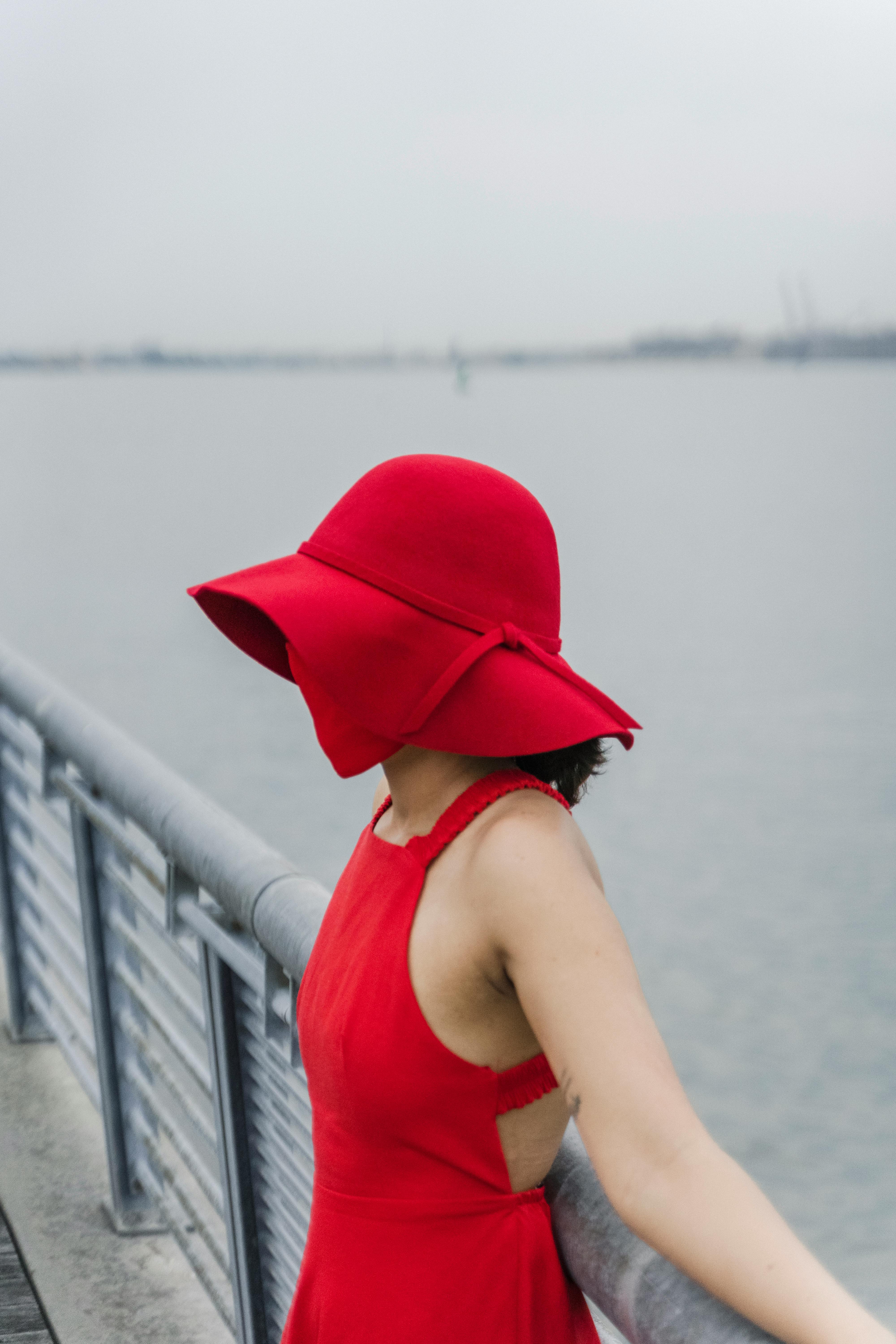 Solitary woman in a red dress and sun hat standing by the waterfront.