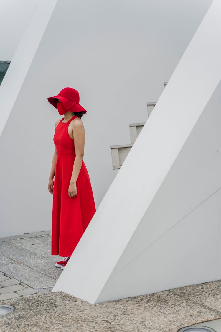 A Woman In A Red Dress And Hat Standing Still