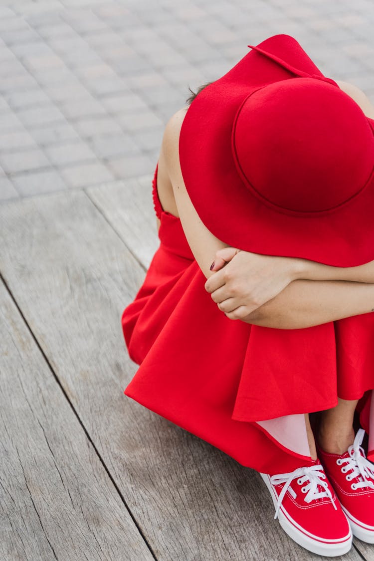 Woman In A Hat Sitting On The Floor Hiding Her Head In Her Arms