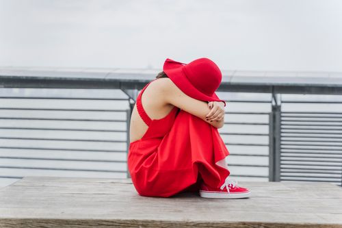 Free A woman in a red dress and hat sitting alone on a wooden bench outdoors. Stock Photo