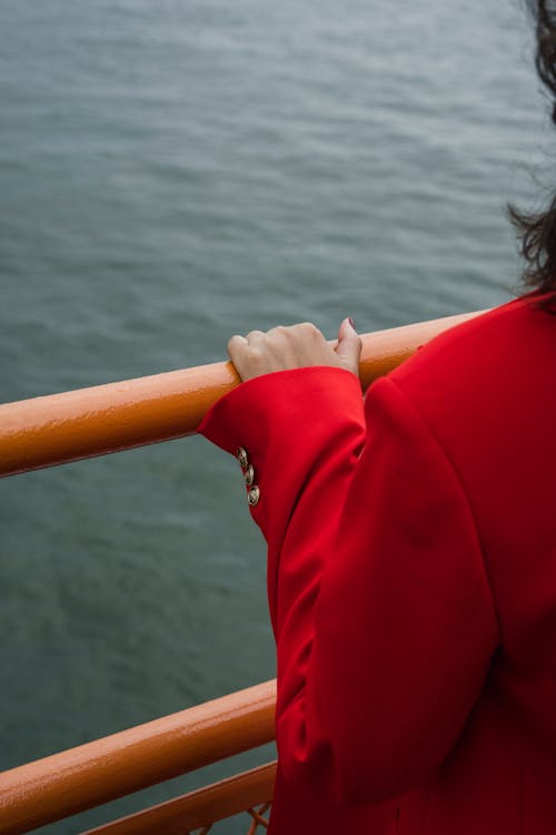 Person in Red Blazer Holding Orange Handrail near the Sea