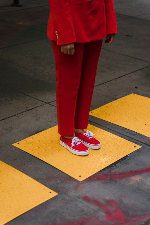 Free Person in bold red outfit stands on urban sidewalk with yellow tiles. Stock Photo