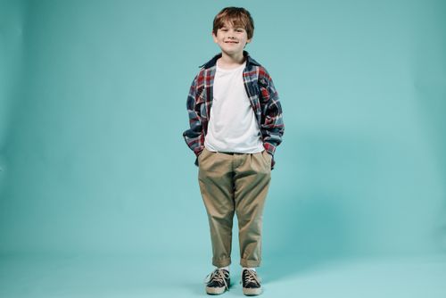 Free Smiling young boy in plaid shirt standing with hands in pockets against blue background. Stock Photo