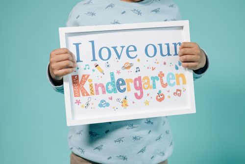 Free A child holding a colorful educational sign displaying 'I love our Kindergarten' message. Stock Photo