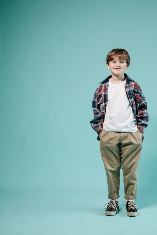 Free Portrait of a smiling child in a plaid shirt with hands in pockets against a blue background. Stock Photo