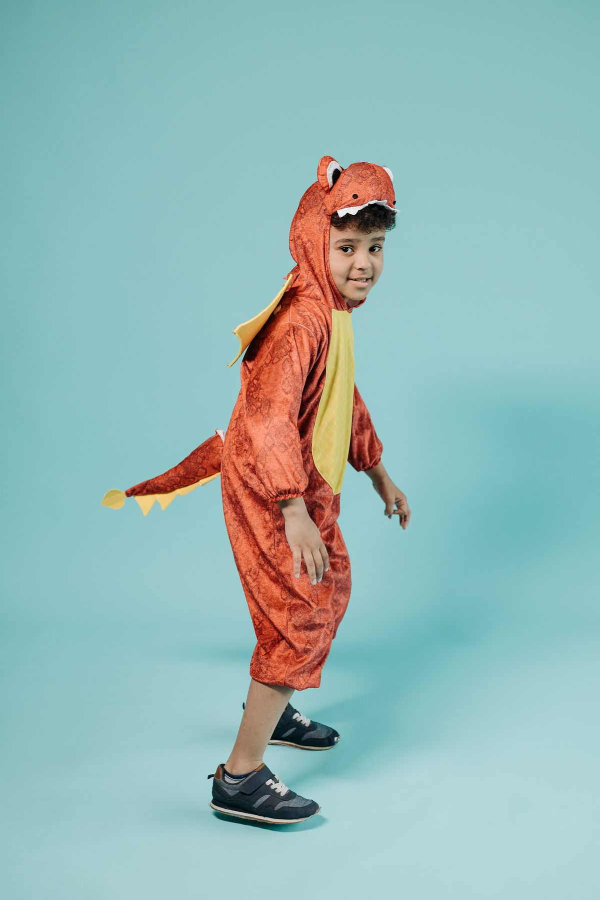 Joyful child in a vibrant dinosaur costume posing in a studio with a playful smile. Stock Photo.